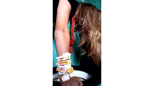 Eine Person trägt bunte Süßigkeitenarmbänder und rote Schnüre am Arm.
