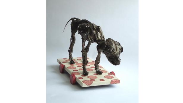 Eine Skulptur eines Hundes steht auf einem Wagen, der mit Wurstscheiben bedeckt ist.
