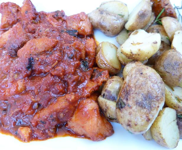 Schweinefleisch in Tomatensauce mit Bratkartoffeln auf einem Teller.