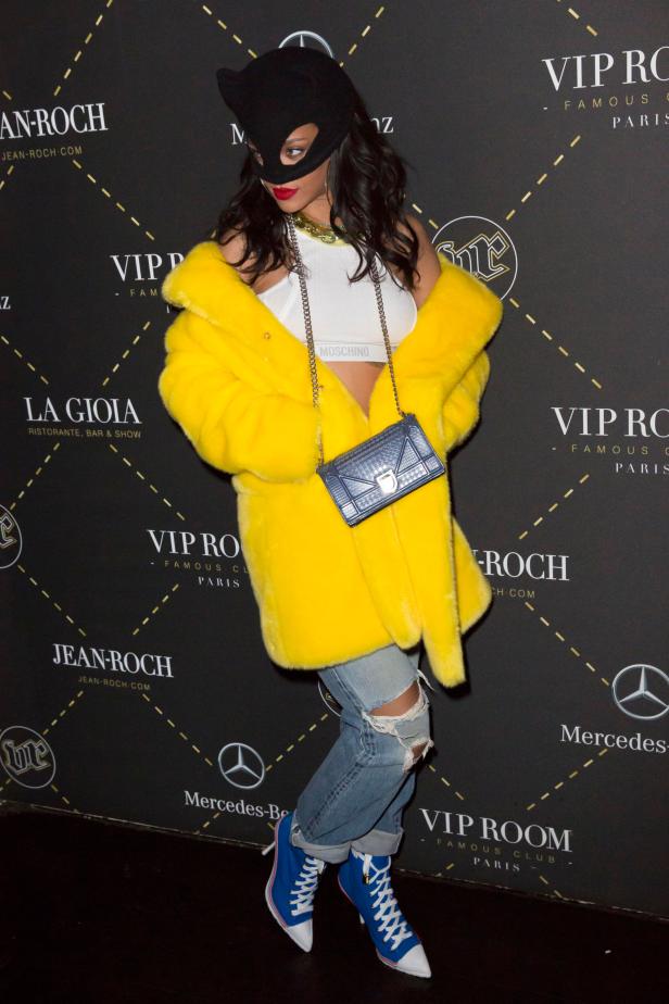 Rihanna mit Katzenmaske, gelbem Mantel und blauen High-Heel-Sneakers bei einer Veranstaltung.