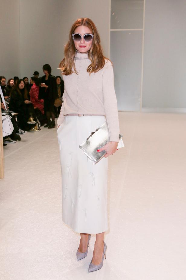 Olivia Palermo trägt einen cremefarbenen Rollkragenpullover und einen weißen Rock mit silberner Clutch.