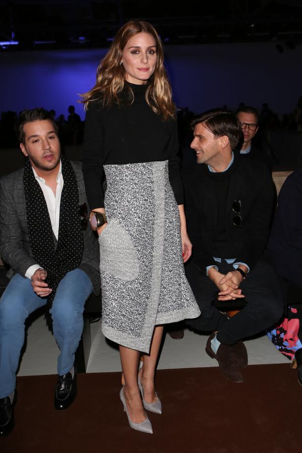 Olivia Palermo posiert bei einer Modenschau zwischen zwei Männern.