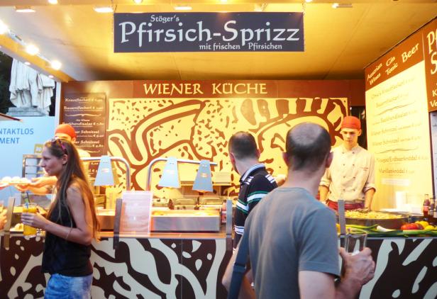 Ein Stand mit „Wiener Küche“ und „Pfirsich-Sprizz“ bietet Speisen und Getränke an.