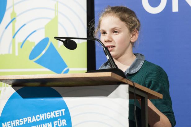 Ein junges Mädchen spricht an einem Rednerpult vor einem blauen Hintergrund.