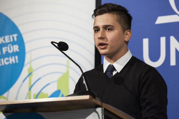 Ein junger Mann spricht an einem Rednerpult vor einem Publikum.