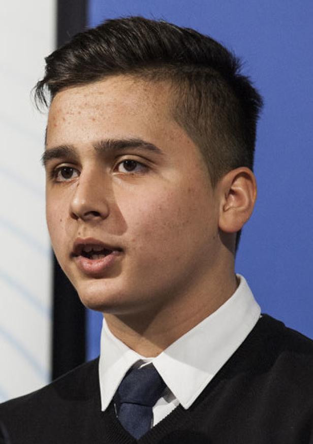 Ein junger Mann mit dunklen Haaren und einem Hemd mit Krawatte spricht.