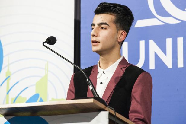 Ein junger Mann spricht an einem Rednerpult vor einem blauen Hintergrund mit dem Schriftzug „UNI“.