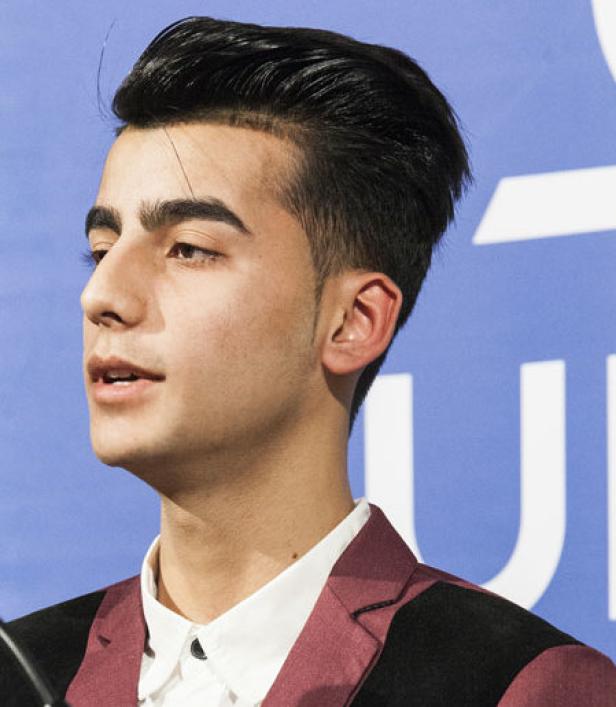 Ein junger Mann mit dunklen Haaren und einem burgunderfarbenen Sakko blickt zur Seite.