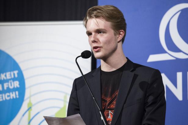 Ein junger Mann spricht bei einer Veranstaltung in ein Mikrofon.