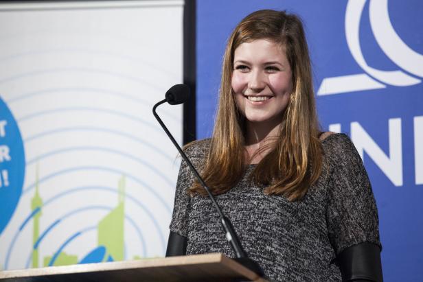 Eine junge Frau lächelt an einem Rednerpult mit Mikrofon.