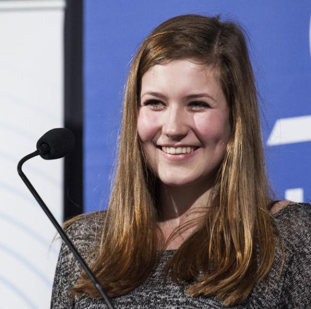 Eine lächelnde junge Frau steht an einem Mikrofon.