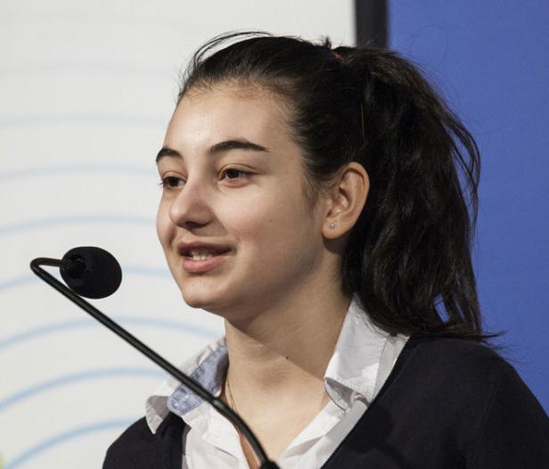 Eine junge Frau spricht bei einer Veranstaltung in ein Mikrofon.