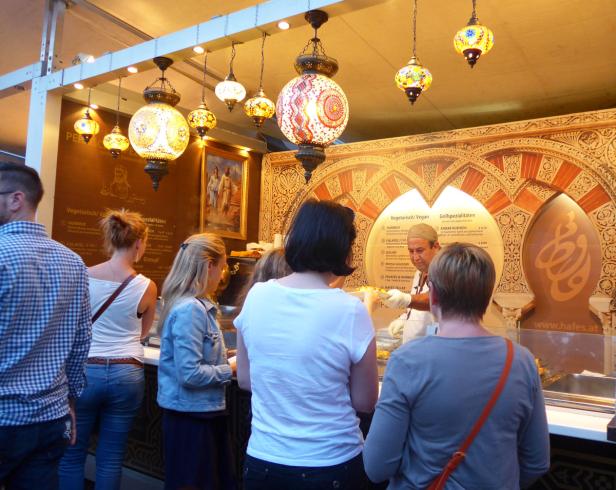 Kunden stehen an einem Stand mit orientalischen Lampen und bestellen Speisen.