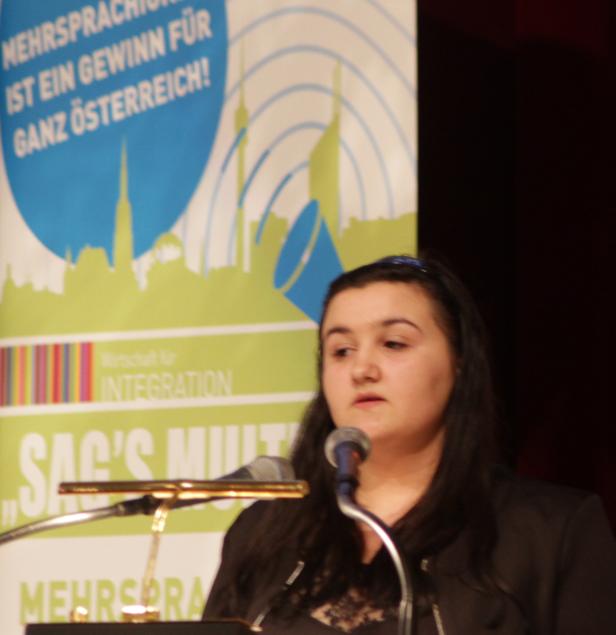 Eine Frau spricht bei einer Veranstaltung vor einem Banner zum Thema Mehrsprachigkeit.