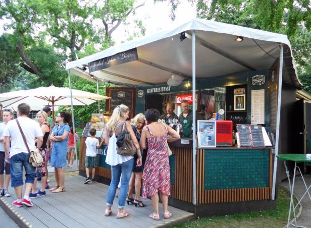 Menschen stehen an einem Imbissstand namens „Gasthaus Hansy“.