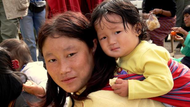 Eine Frau trägt ein kleines Kind auf dem Rücken.