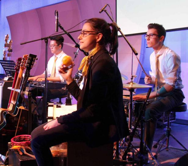 Eine Band spielt auf der Bühne, eine Frau hält eine Orange in der Hand.