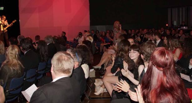 Ein Publikum applaudiert einer Sängerin und einer Band auf einer Bühne.