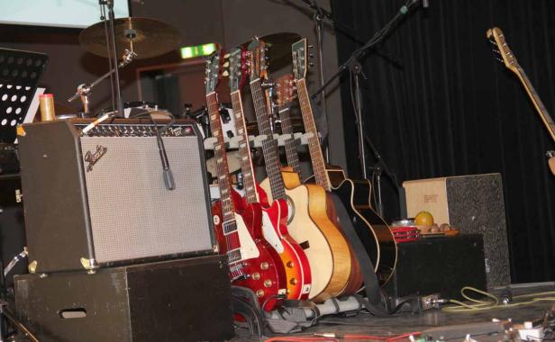 Auf einer Bühne stehen mehrere Gitarren, ein Verstärker und Schlaginstrumente.