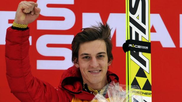 Ein lächelnder Skispringer mit geballter Faust und Ski der Marke Fischer.