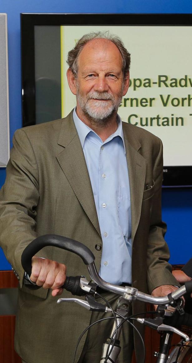 Hat den Vorsitz im Verkehrsausschuss: Michael Cramer von den Grünen Ein Mann im Anzug hält ein Fahrrad.