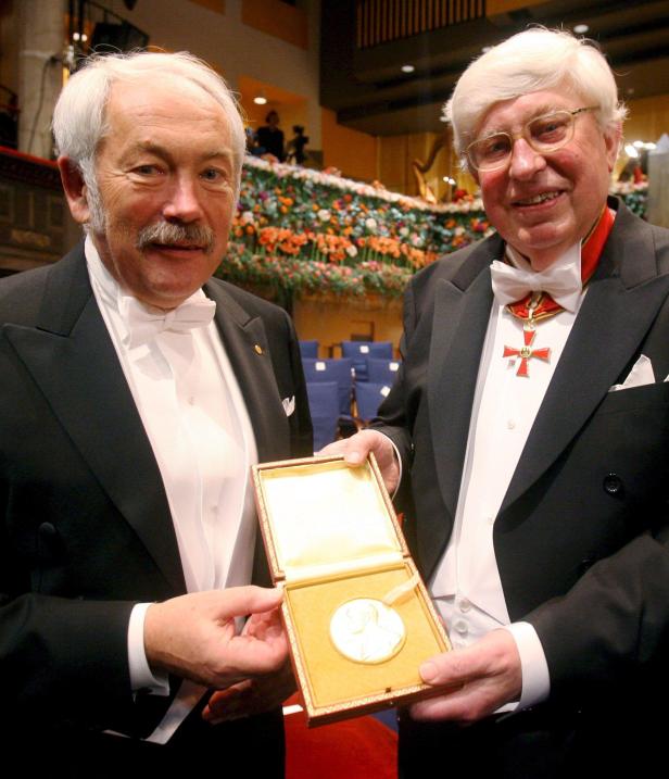 Zwei Männer im Smoking präsentieren eine Medaille in einer Schatulle.