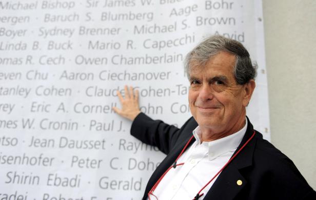 Ein Mann zeigt auf eine Wand mit Namen von Nobelpreisträgern.