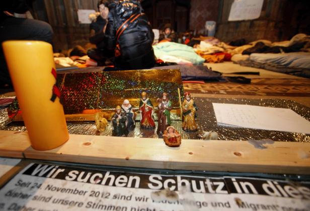 Eine Krippe steht vor einem Transparent mit der Aufschrift „Wir suchen Schutz in...“.