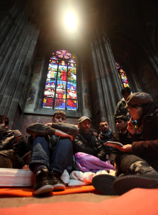 Eine Gruppe von Menschen sitzt vor einem bunten Glasfenster in einer Kirche.
