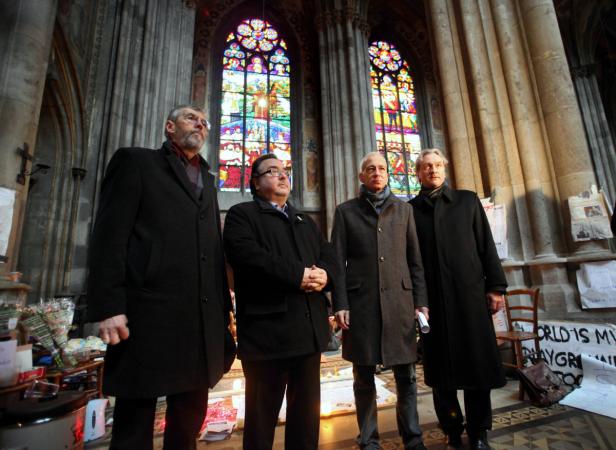 Vier Männer stehen in einer Kirche vor bunten Glasfenstern.