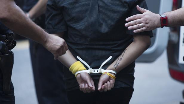 Eine Person wird von Polizisten mit Kabelbindern gefesselt.