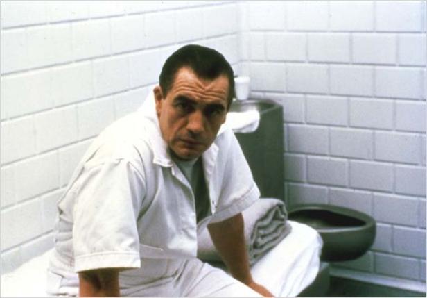 Ein Mann in weißer Anstaltskleidung sitzt in einer Zelle.