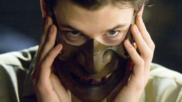 Ein Mann hält eine Maske vor sein Gesicht.