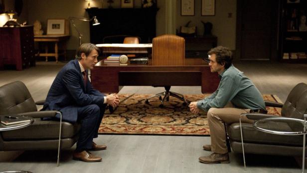 Mads Mikkelsen und Hugh Dancy sitzen sich in einer Szene aus der Fernsehserie „Hannibal“ gegenüber.
