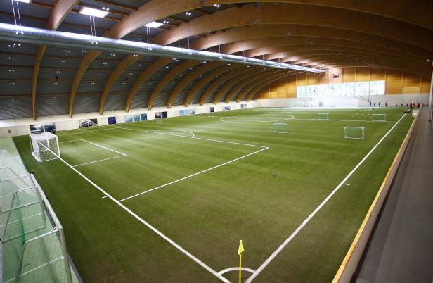 Eine große, leere Indoor-Fußballhalle mit Kunstrasen und Holzbalkendecke.