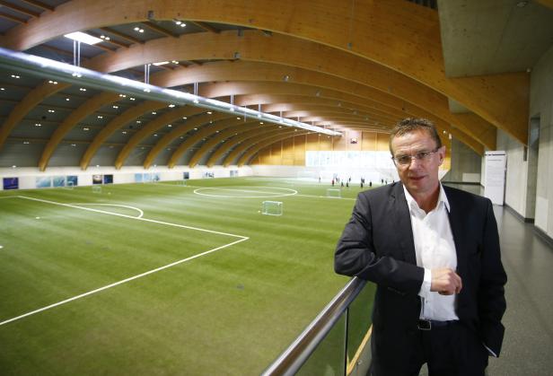 Ein Mann in Anzug steht vor einer großen Indoor-Fußballhalle.