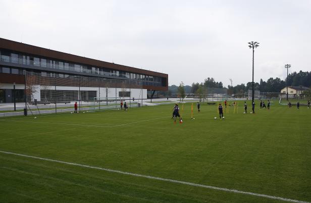 Fußballspieler trainieren auf einem grünen Rasenplatz vor einem modernen Gebäude.