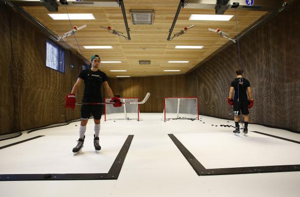 Zwei Hockeyspieler trainieren in einer Halle mit Kunsteisfläche.