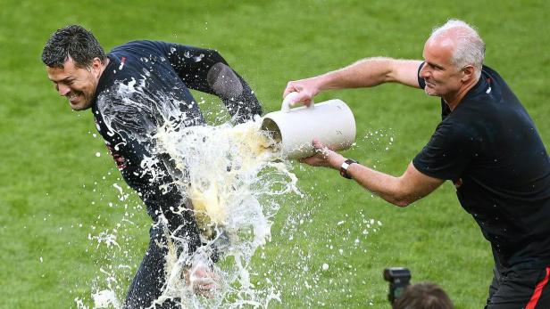Ein Mann schüttet einem anderen Mann auf einem grünen Rasen Bier über den Kopf.