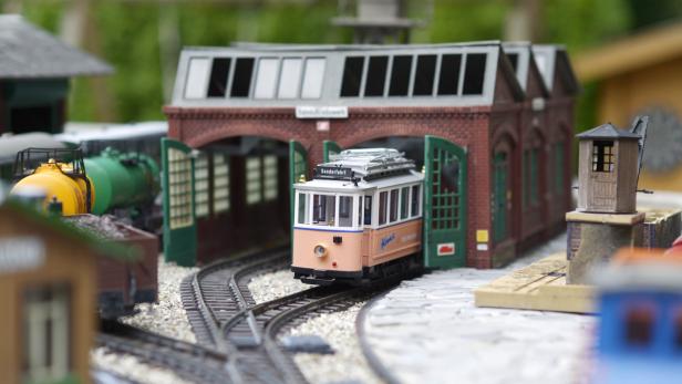 Eine Modellstraßenbahn steht vor einem Backsteindepot mit geöffneten grünen Toren.