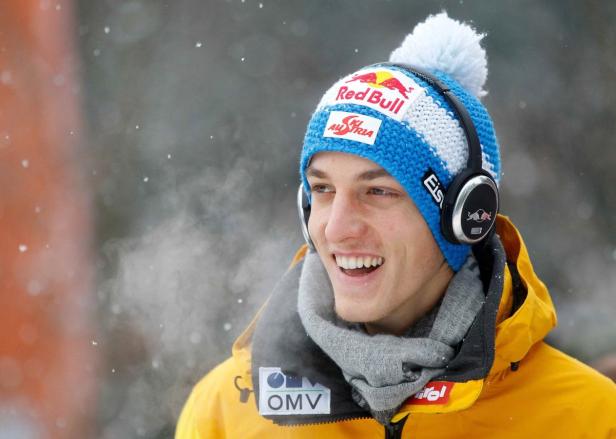 Ein lächelnder Mann mit Mütze und Kopfhörern im Schnee.