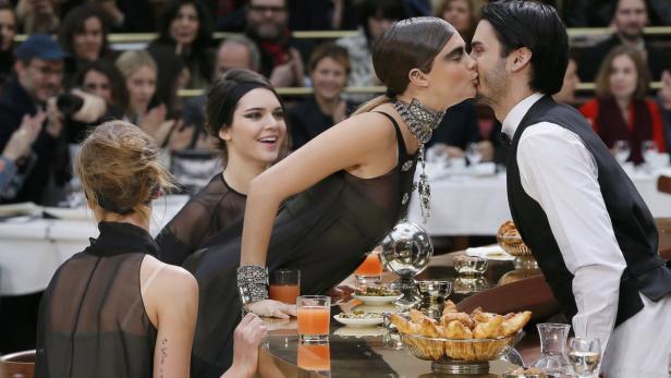 Cara Delevingne küsst einen Kellner, während Kendall Jenner danebensteht und lächelt.
