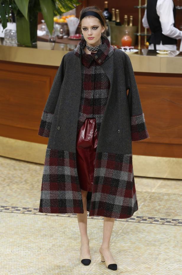 Eine Frau in einem langen Mantel mit Karomuster und einem roten Rock.