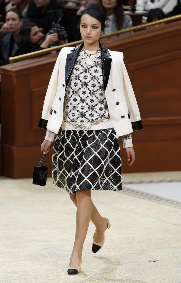 Eine Frau in einem gemusterten Rock und einer Jacke auf einem Laufsteg.