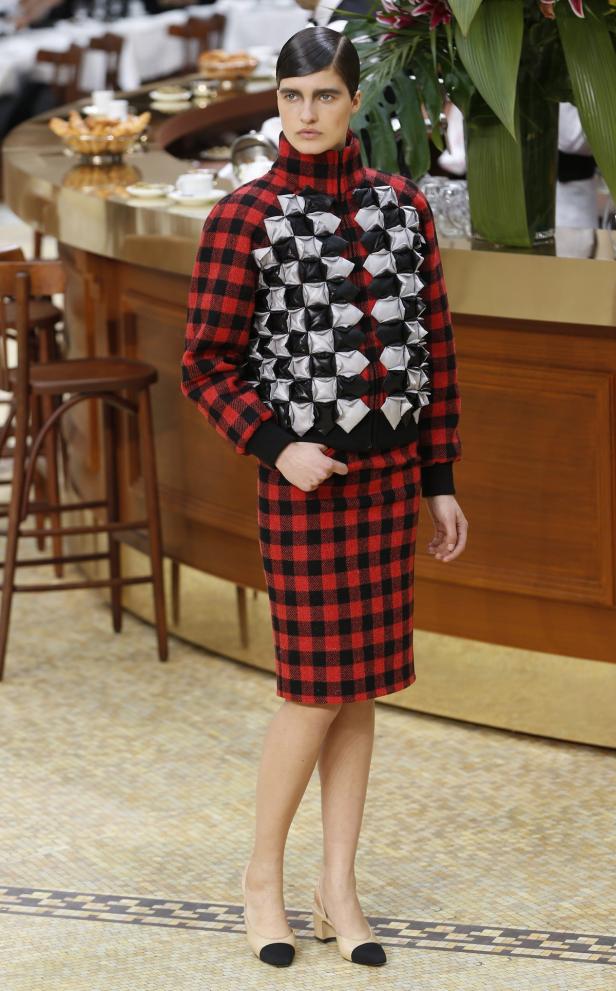 Eine Frau in einem rot-schwarz karierten Kostüm mit einer Jacke mit geometrischen Verzierungen.