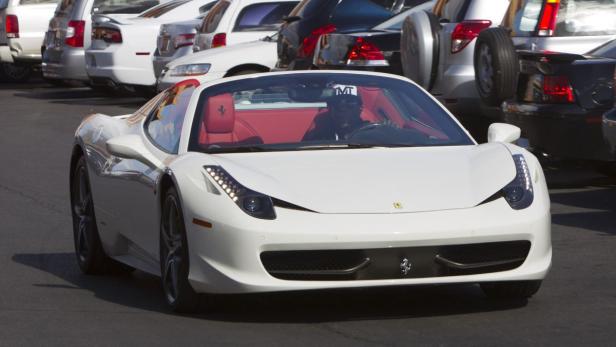 Ein weißer Ferrari 458 Spider mit roter Innenausstattung fährt auf einer Straße.