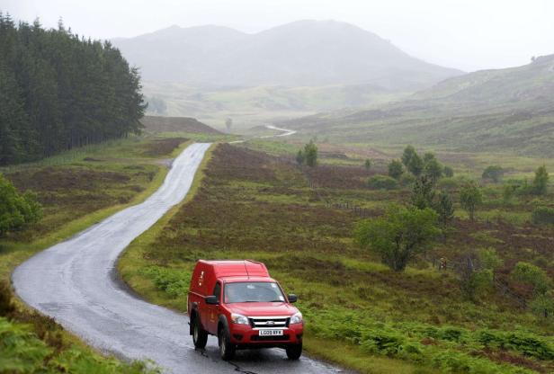 Ein Postzusteller in Highland Perthshire, Schottland Ein roter Postwagen fährt auf einer kurvenreichen Straße durch eine hügelige Landschaft.