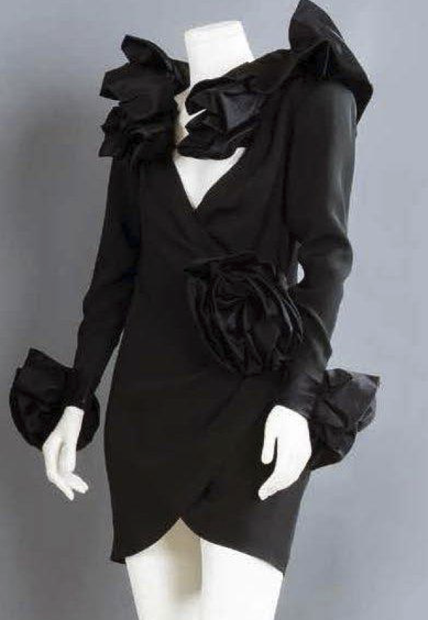 Ein schwarzes Kleid mit Rüschen und einer großen Stoffblume auf einer Schneiderpuppe.