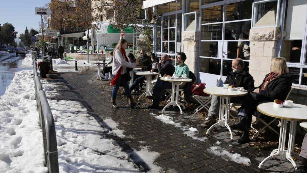 Gäste sitzen an Tischen vor einem Café an einem Wintertag mit Schnee auf dem Bürgersteig.