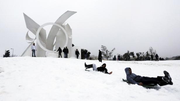 Menschen rodeln im Schnee vor einer abstrakten Skulptur.